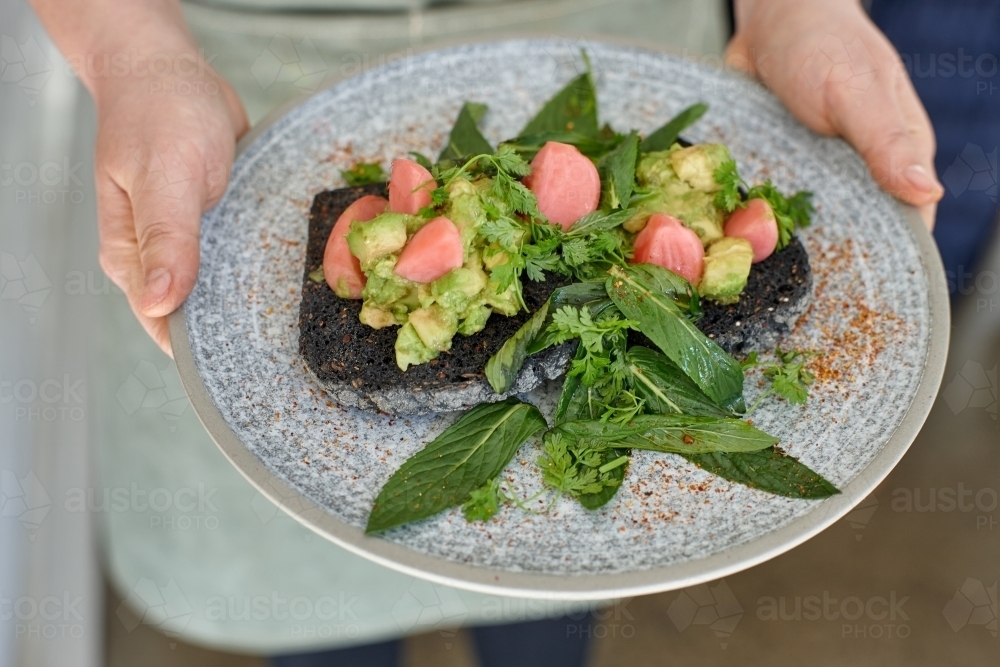 Waiter holding healthy avocado on toast meal on plate - Australian Stock Image
