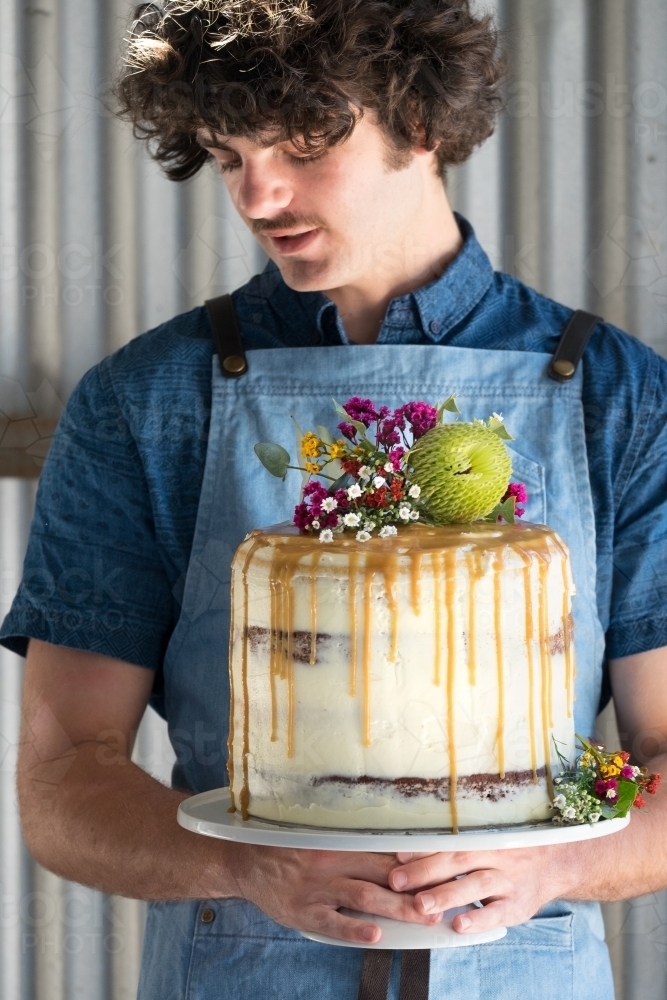 Waiter holds wedding cake decorated with wildflowers - Australian Stock Image