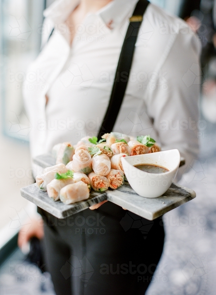 Waitress carrying platter of rice paper rolls and dipping sauce - Australian Stock Image