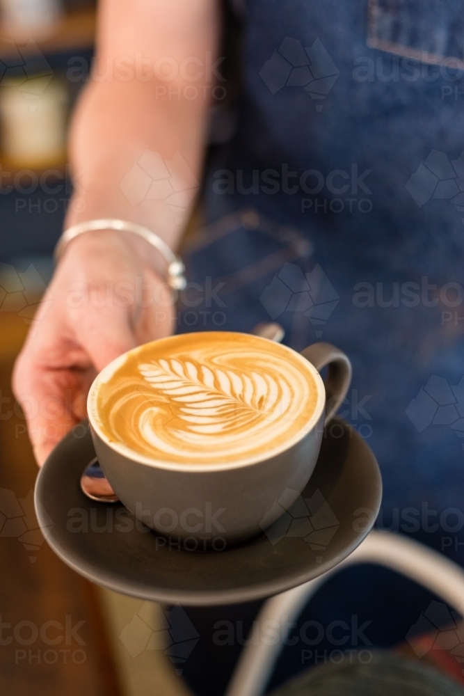 waitress holding flat white with pretty coffee art rosetta - Australian Stock Image
