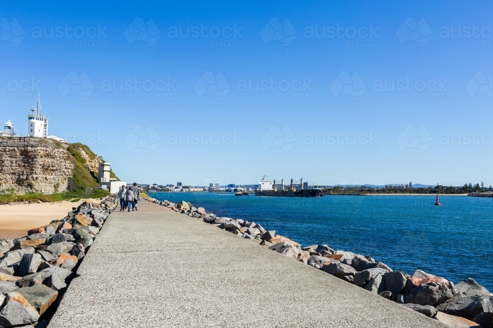 walking along Newcastle breakwater on sunlit day with ship leaving port - Australian Stock Image