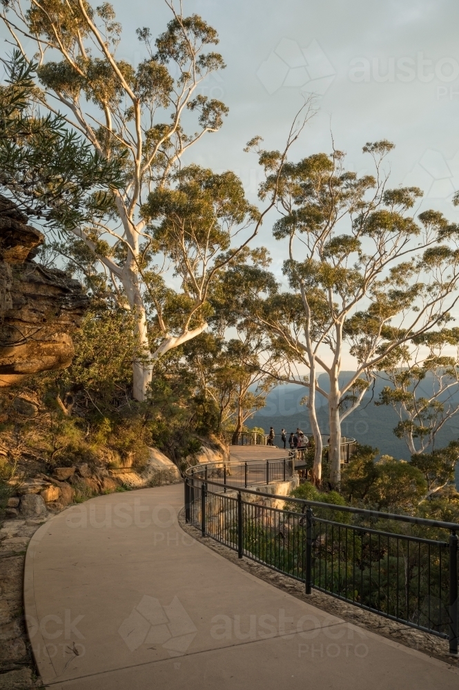 Walking path in bushland with safety fence, gumtrees and distant walkers - Australian Stock Image