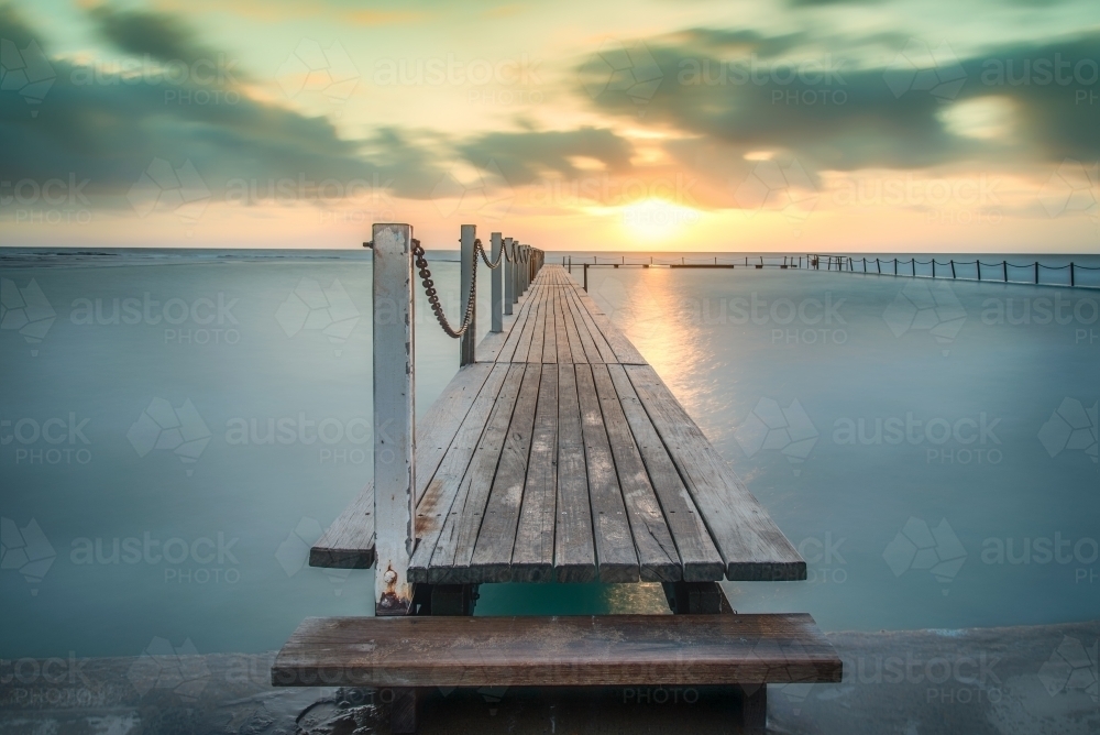 Warm sunrise over coastal rock pool with timber walkway - Australian Stock Image