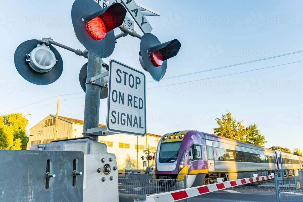 Warning lights flashing while a commuter train speeds through a railway crossing - Australian Stock Image