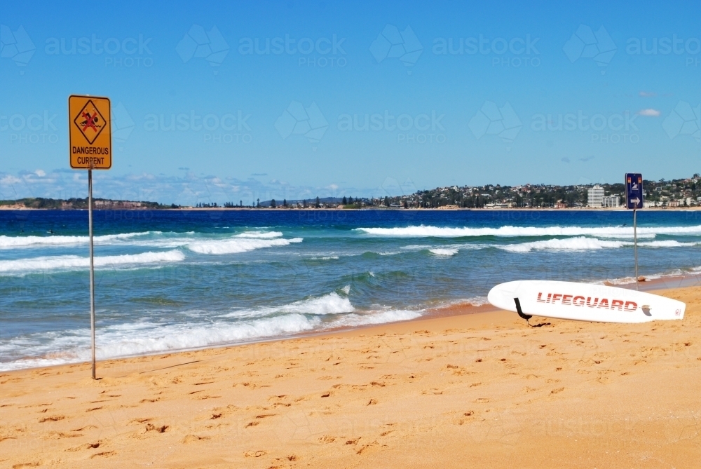Warning sign and lifeguard surfboard on a beach in Sydney - Australian Stock Image