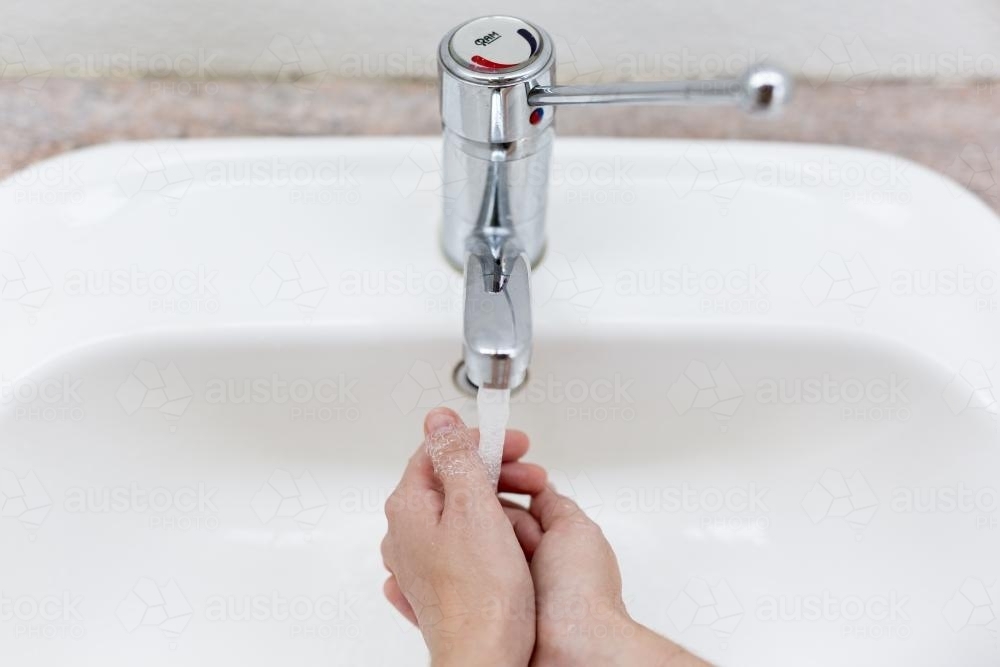 Washing hands in a public bathroom. - Australian Stock Image