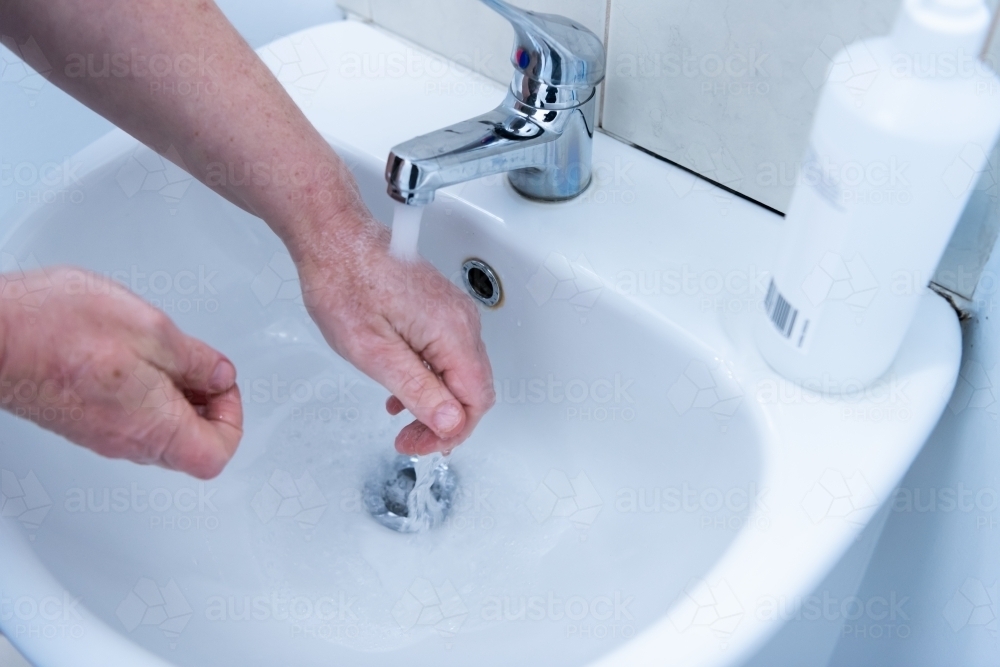 Washing hands with soap and water at basin - Australian Stock Image