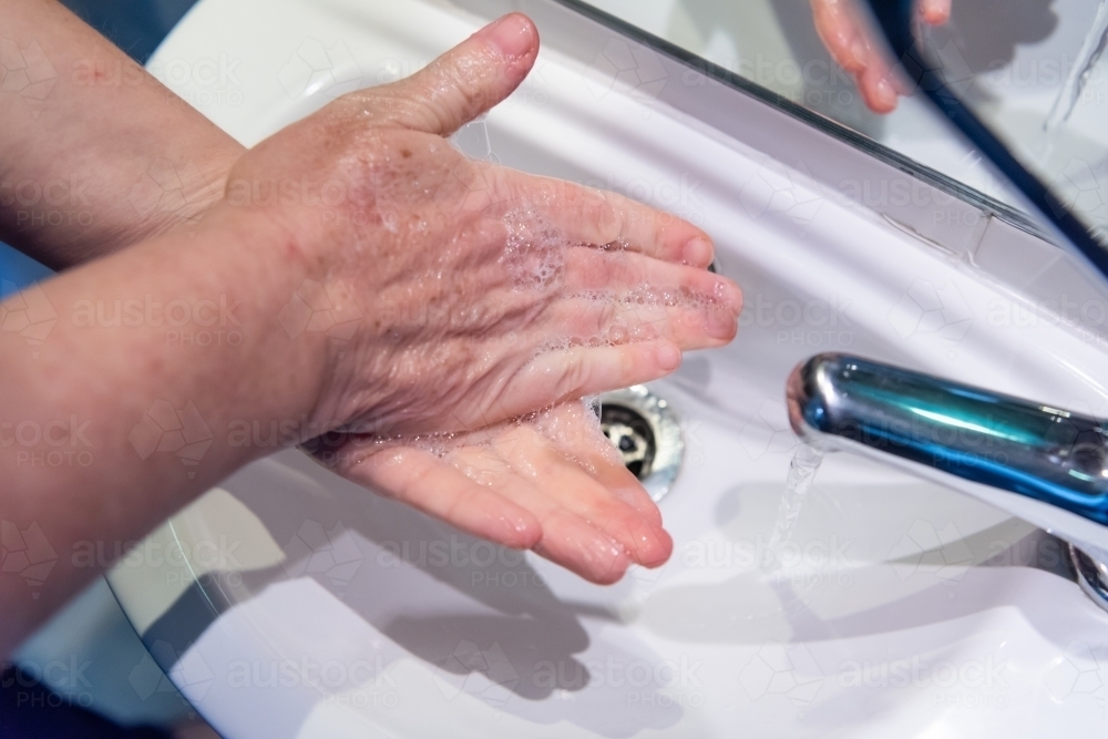 Washing hands with soap and water at basin - Australian Stock Image