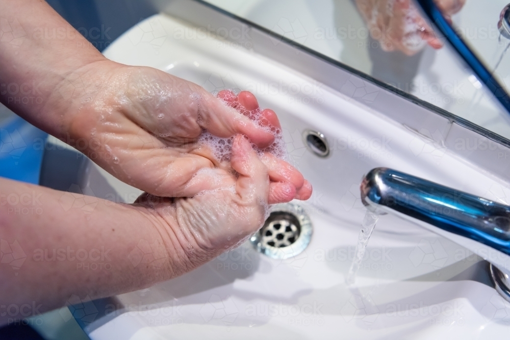 Washing hands with soap and water at basin - Australian Stock Image