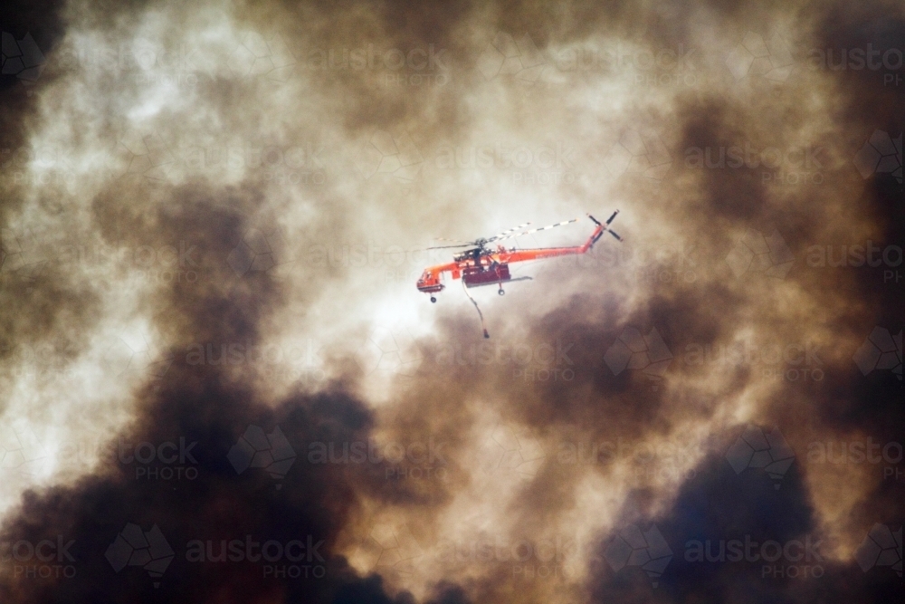 Water-bombing helicopter fighting a bushfire among thick smoke. - Australian Stock Image