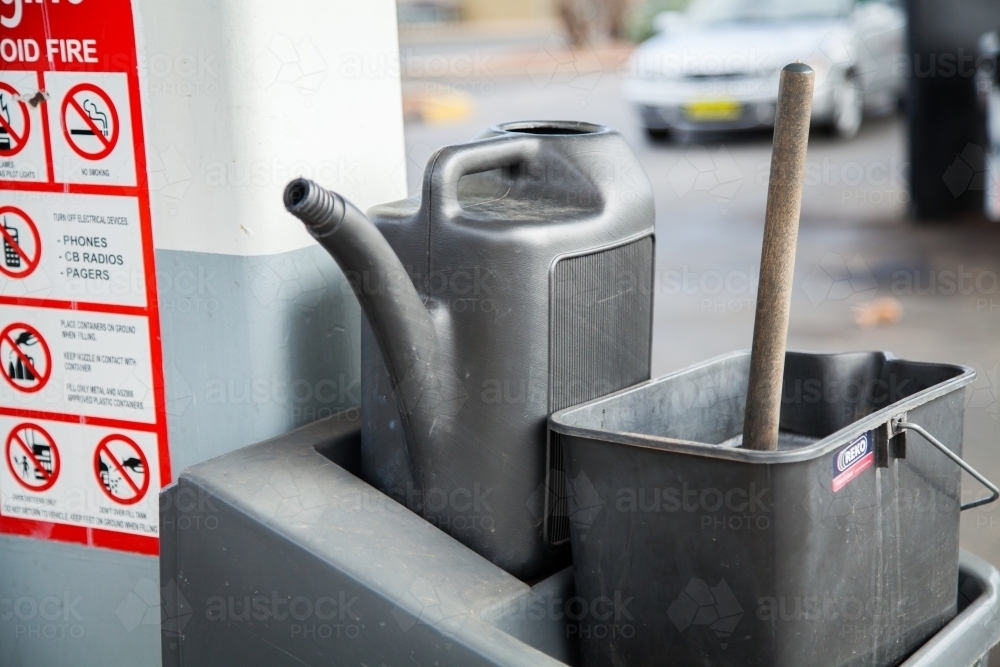 Water can and bucket at petrol station for washing car windscreen - Australian Stock Image