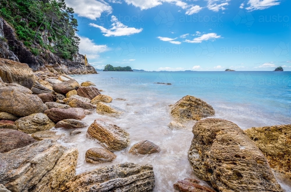 Water crashing on yellow rocks at beautiful beach paradise - Australian Stock Image