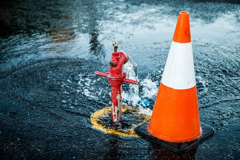 Water flooding the street during road works and orange road cone - Australian Stock Image