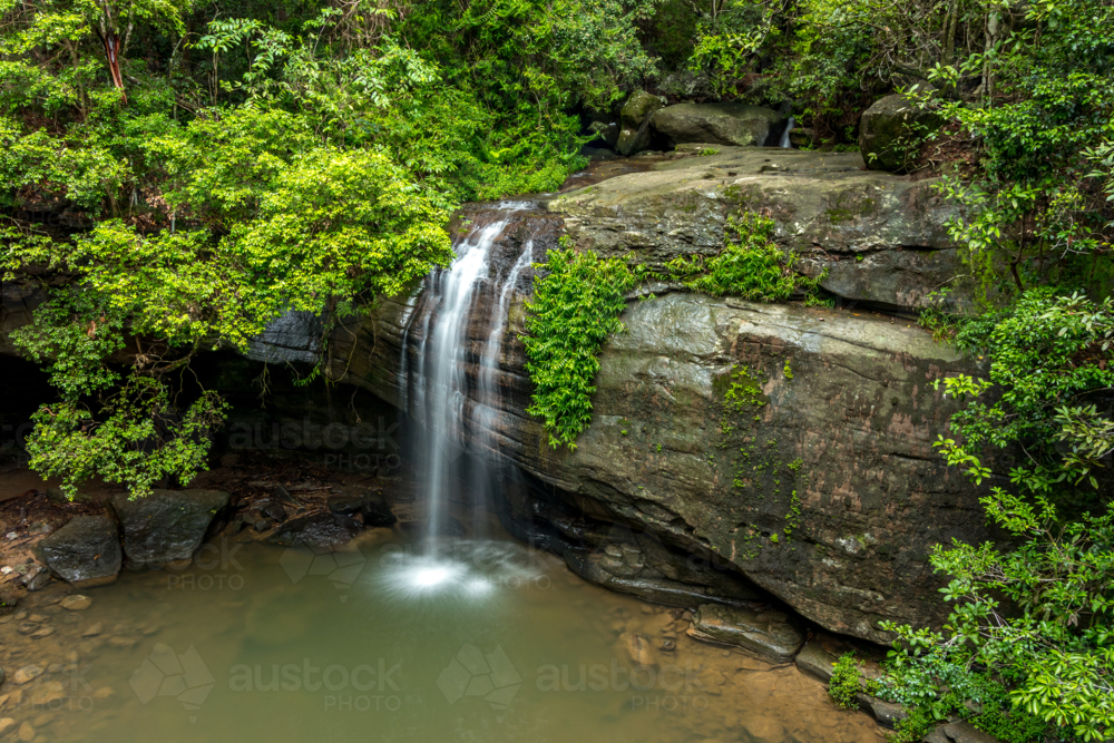 Waterfall over large rock in rainforest taken from above - Australian Stock Image