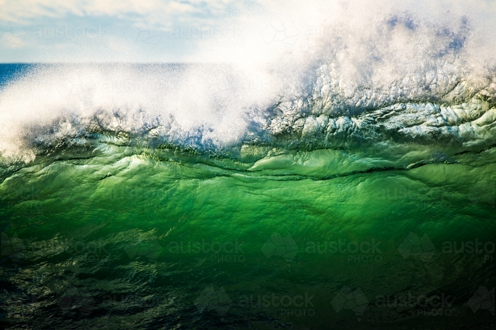 Wave breaking in big surf, green water backlit by sunrise - Australian Stock Image