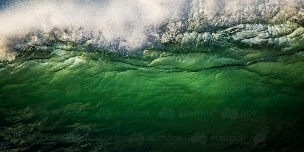 Wave breaking in big surf, green water backlit by sunrise - Australian Stock Image