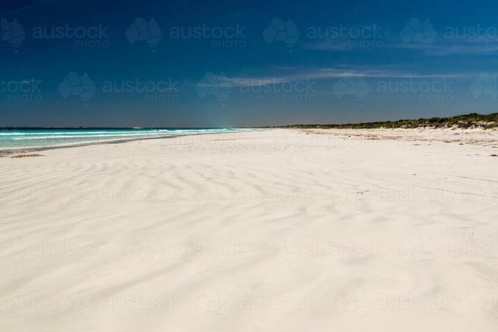 Wave patterns on a white sand beach leading to a far horizon and dark polarised blue sky - Australian Stock Image