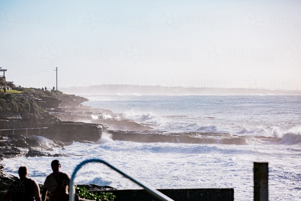 Waves crashing against Cronulla coastline rock at sunrise with sea spray - Australian Stock Image
