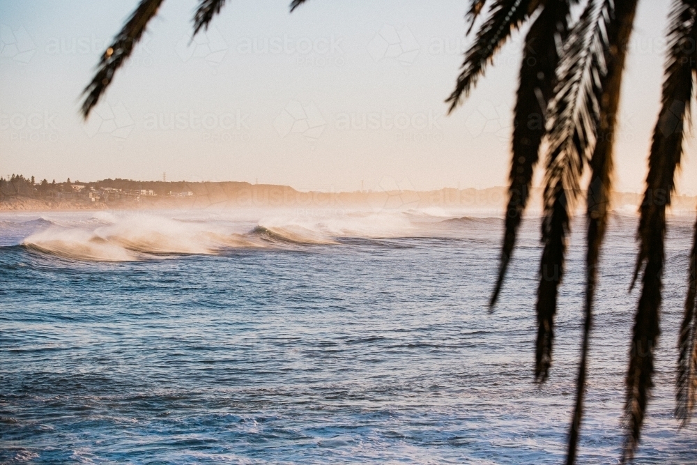 Waves crashing coastline at sunrise with sea spray - Australian Stock Image