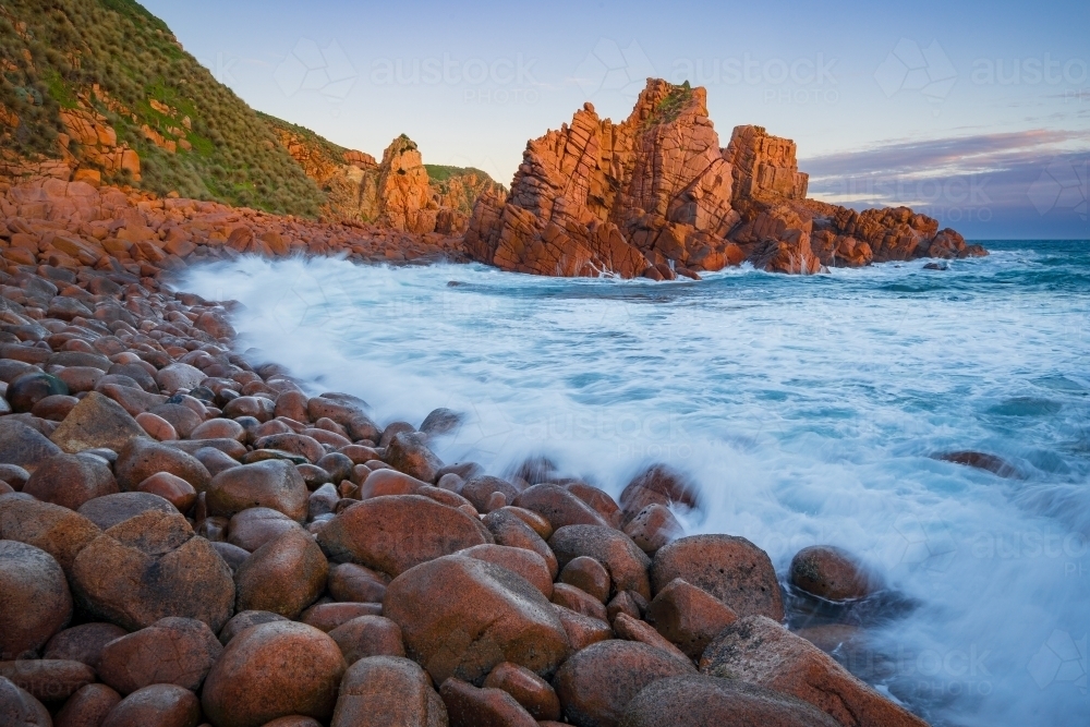 Waves crashing on a rocks along a coastline covered with large boulders and rock formations - Australian Stock Image