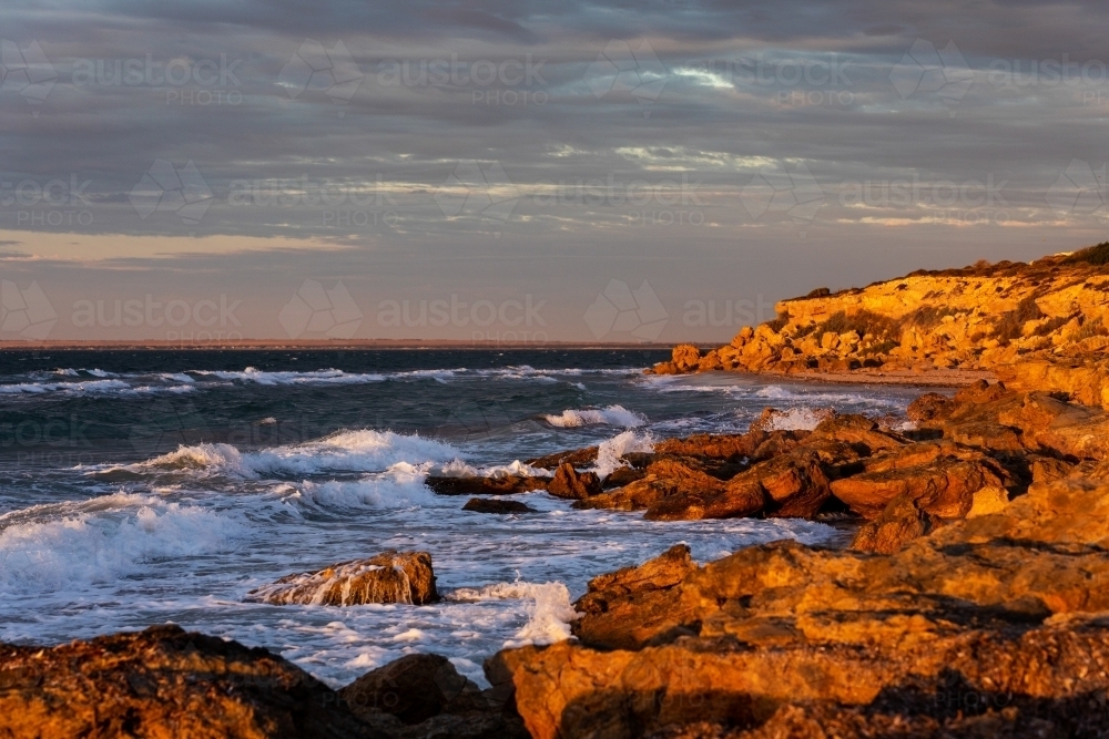 waves crashing on rocks in late afternoon light - Australian Stock Image