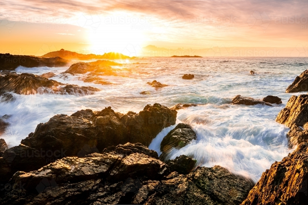 Waves crashing on some rocks at Sawtell Beach at sunrise - Australian Stock Image