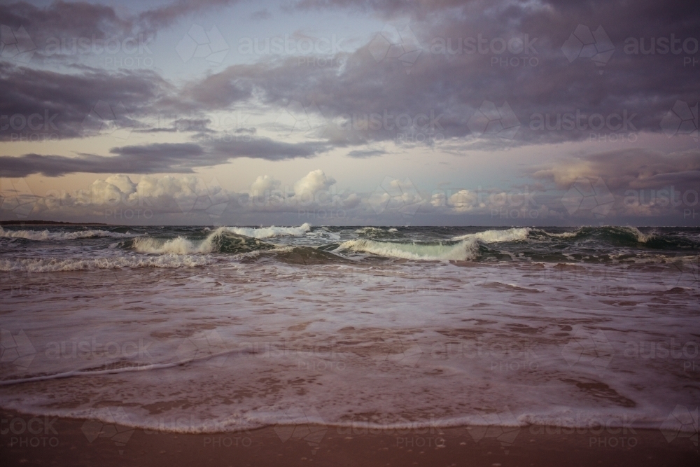 Waves crashing on the beach under a brooding sky - Australian Stock Image