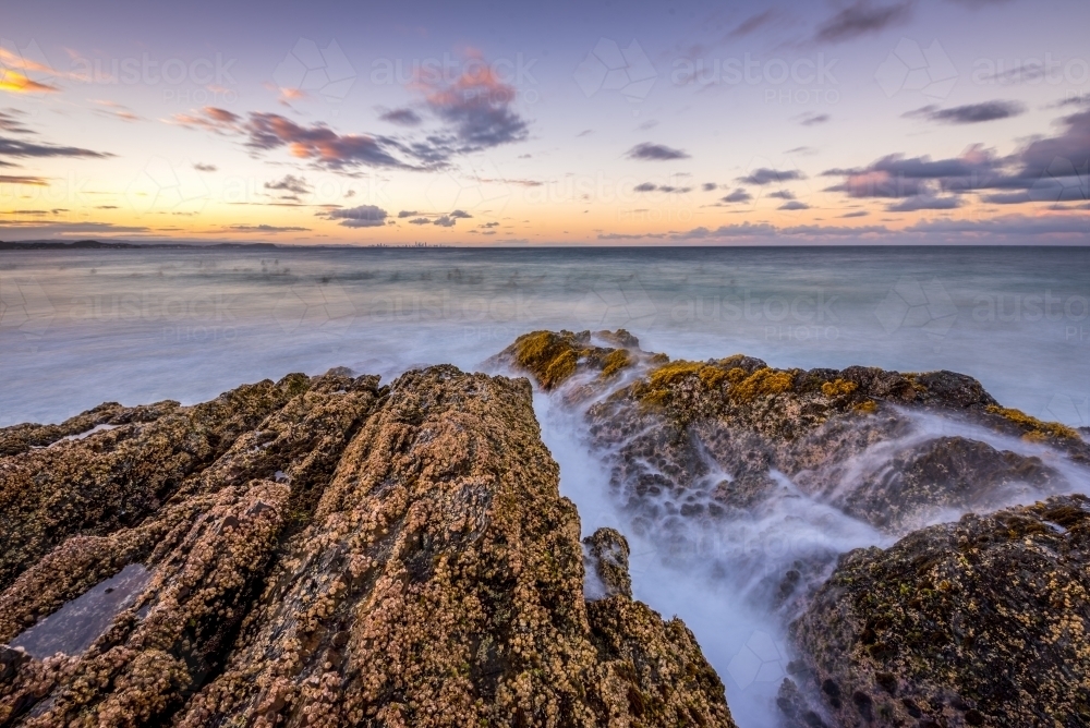 Waves crashing over rocks at sunset - Australian Stock Image