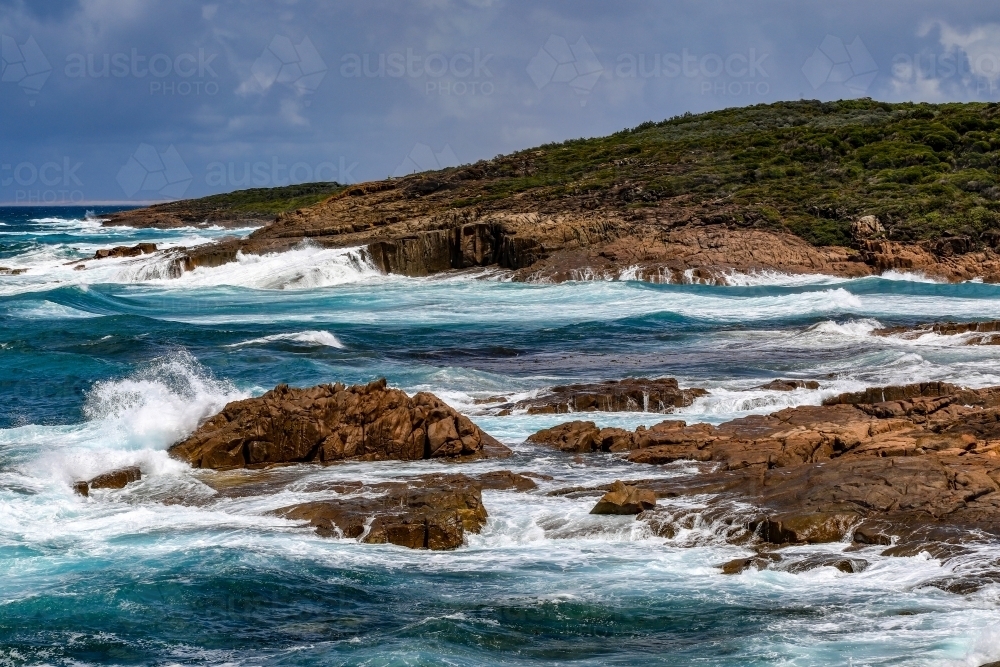 Waves crashing over rocky coastline against cloudy sky - Australian Stock Image