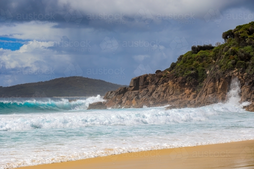 Waves crashing over rocky coastline against cloudy sky - Australian Stock Image