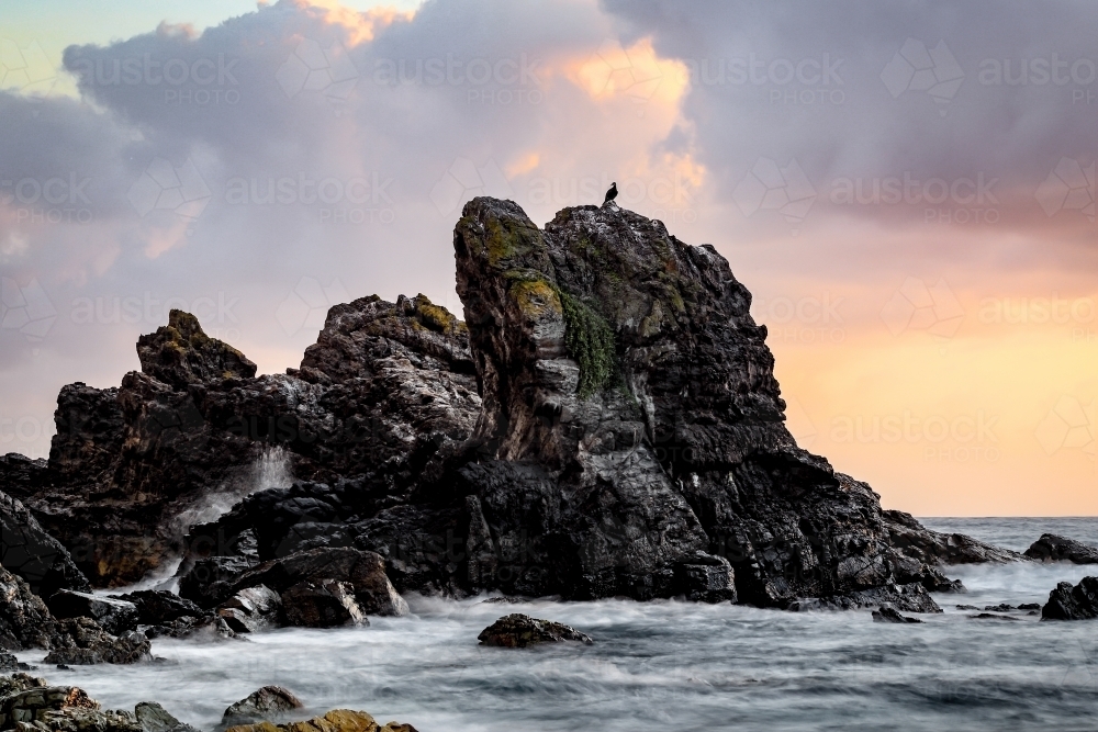 Waves crashing over rocky coastline beneath cloudy sky - Australian Stock Image