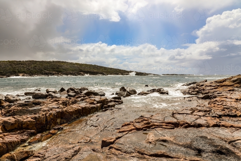 Waves crashing over rocky coastline with cloudy sky - Australian Stock Image