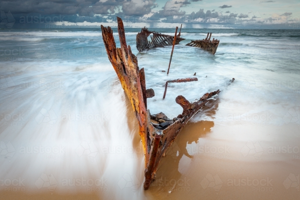 Waves engulfing the bow of a shipwreck on a beach - Australian Stock Image
