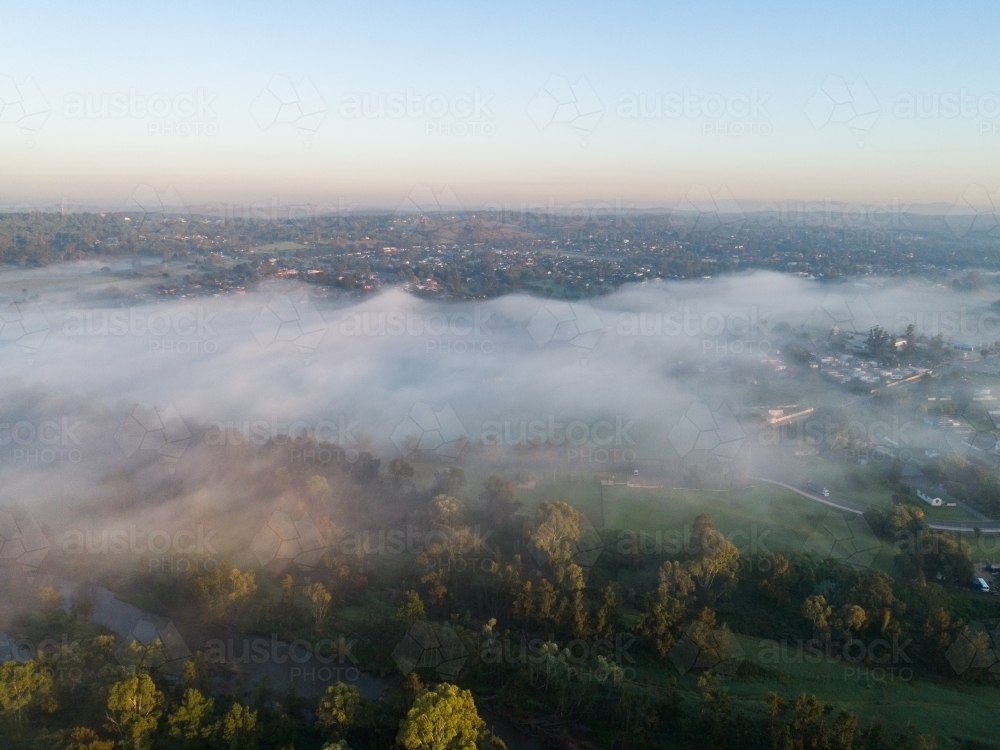 Waves of fog misting over river and rural town of Singleton at dawn - Australian Stock Image