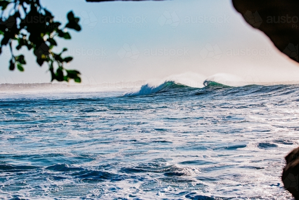 Waves peaks crashing coastline at sunrise with sea spray - Australian Stock Image