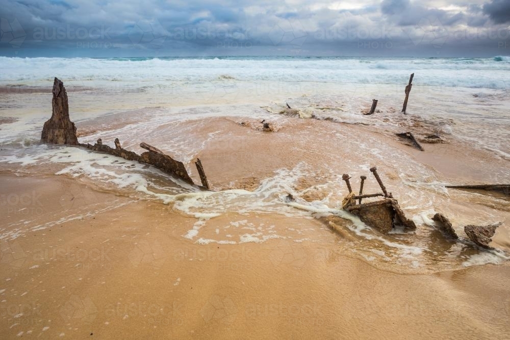 Waves recede over scrap metal pieces of a shipwreck on a beach - Australian Stock Image