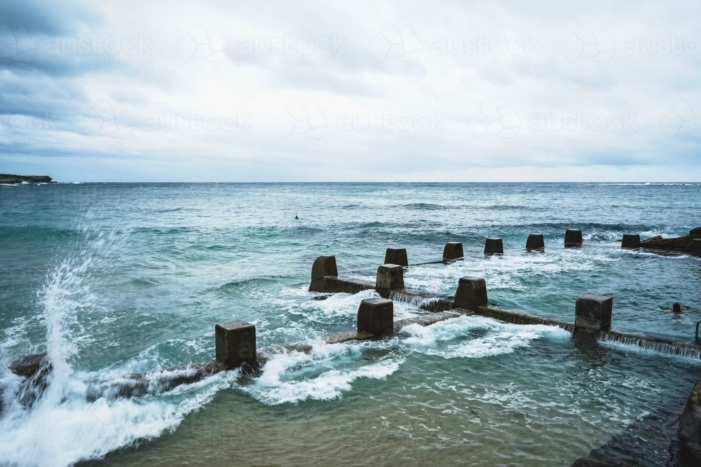 Waves splashing against ocean rock pool in Coogee Sydney on a cloudy day - Australian Stock Image