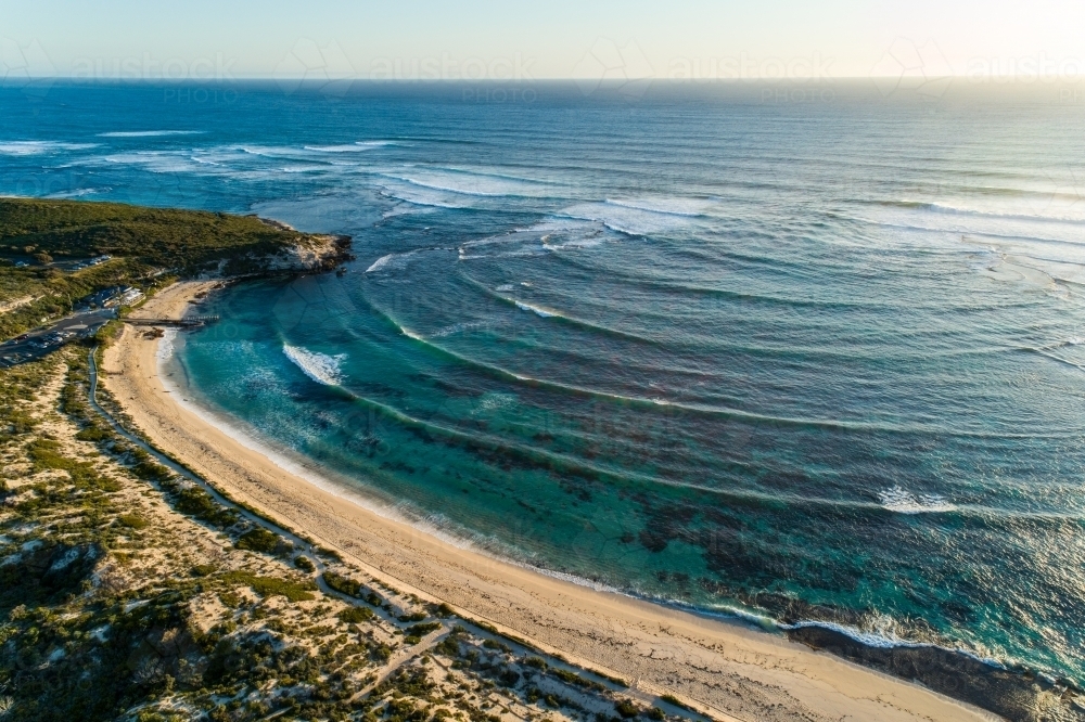 Waves wrapping around a headland in late afternoon light. - Australian Stock Image