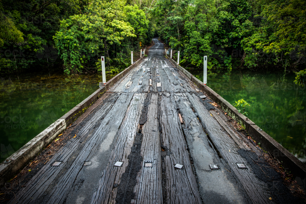Weathered timber bridge over calm green water - Australian Stock Image