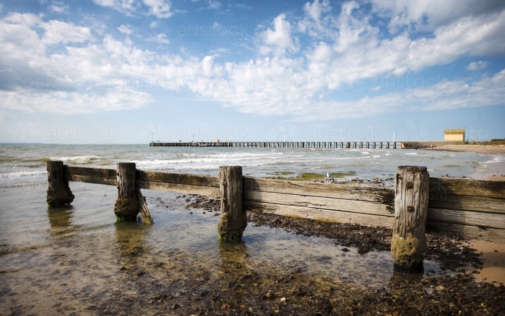 weathered wooden groyne with pier and shed in background - Australian Stock Image