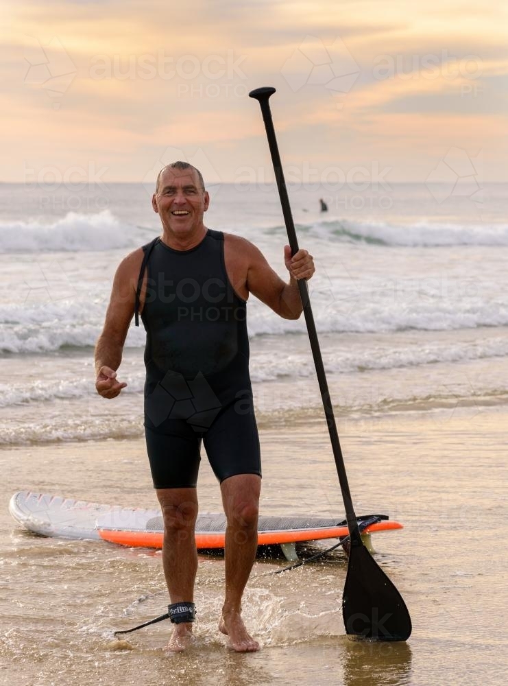 Wet man on beach  holding paddle, laughing and joking - Australian Stock Image