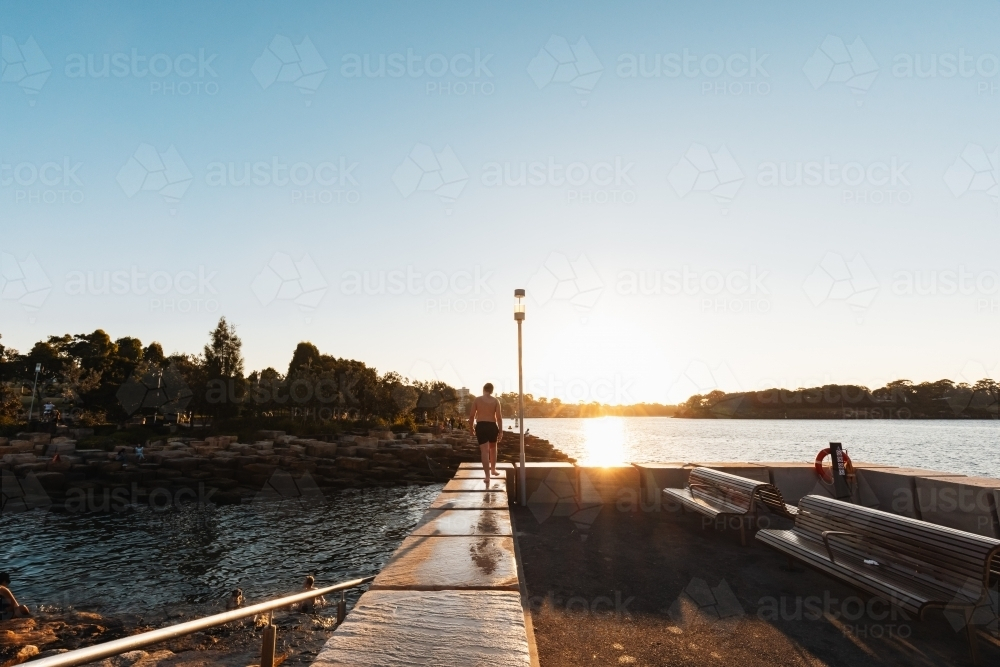 Wet teenager walking along ledge at Marrinawi Cove in bright afternoon sunshine - Australian Stock Image