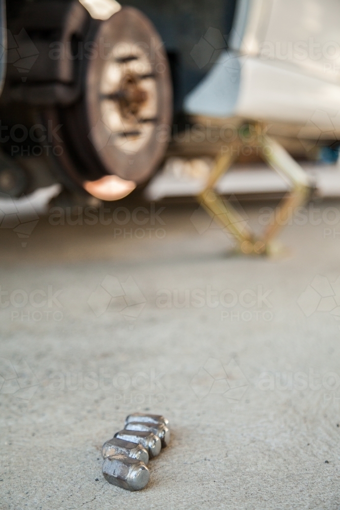 Wheel nuts lying on ground beside jacked up car - Australian Stock Image