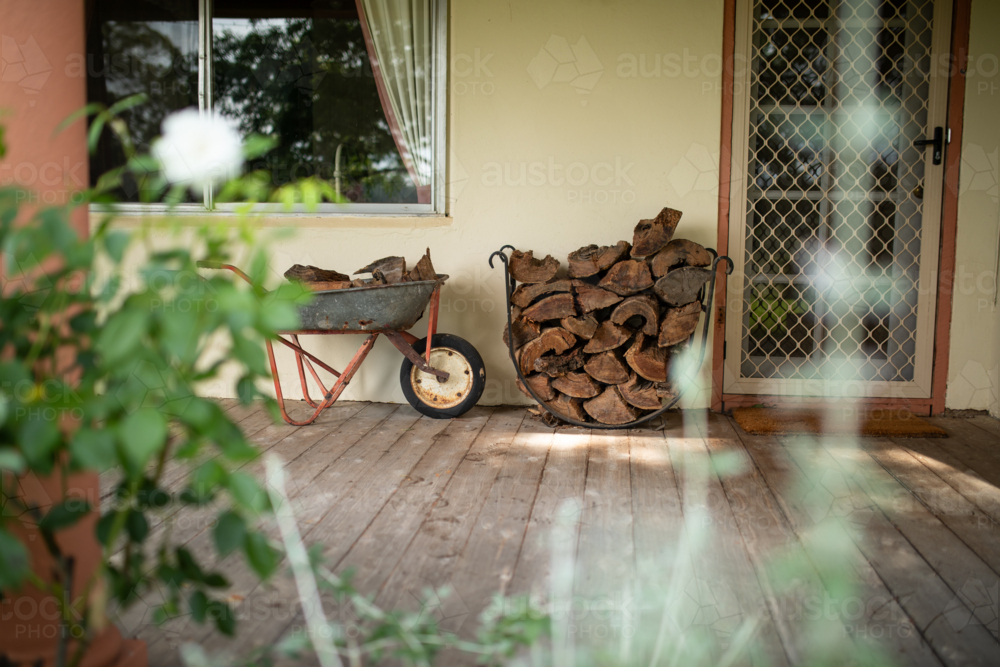 Wheelbarrow and stack of wood on verandah of country home ready for winter - Australian Stock Image