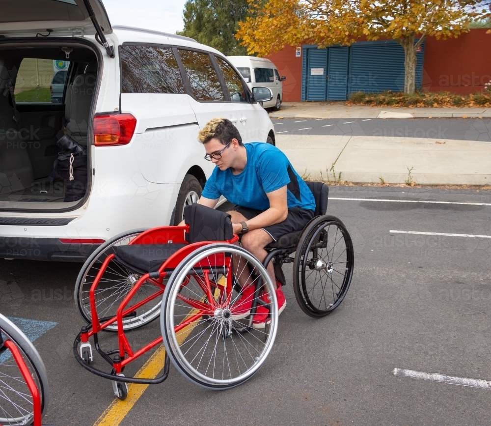 wheelchair athlete folding wheelchair to put into car - Australian Stock Image