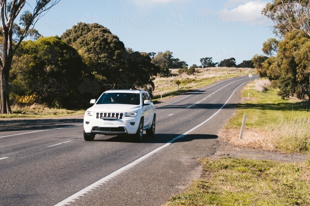 Image of White 4WD car travelling on country road Austockphoto