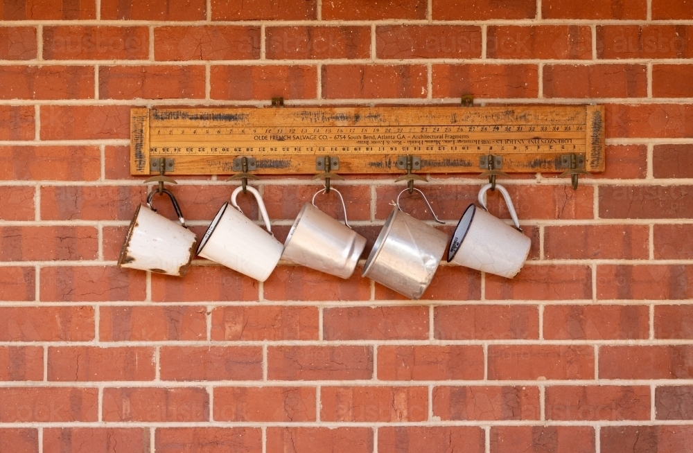 white and silver tin mugs hanging on red brick wall - Australian Stock Image