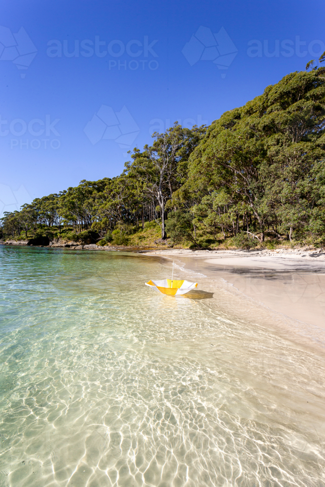 White and yellow beach umbrella upside down on the shoreline - Australian Stock Image