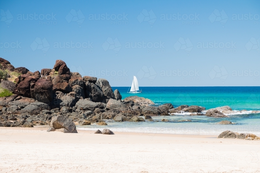White boat sailing the clear blue seas off sandy beach - Australian Stock Image