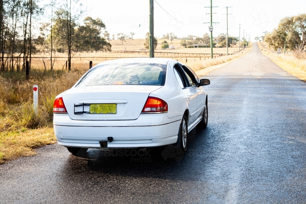 White car driving on wet country road after rain - Australian Stock Image